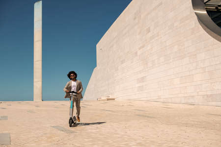 Energetic African American man riding electric scooter. Man with curly hair with sunglasses spending...