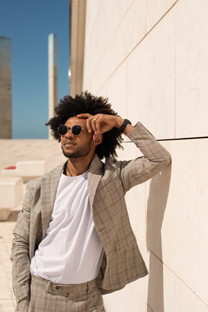 Portrait of cool man outdoors. African American man in suit with beard leaning on wall, walking. Portrait, city life conceptの写真素材