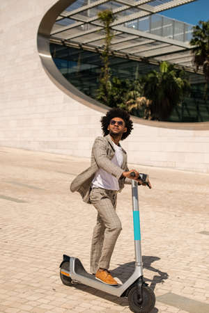 Happy African American man riding electric scooter. Man with curly hair with sunglasses spending time outdoors. Technology, activity conceptの写真素材