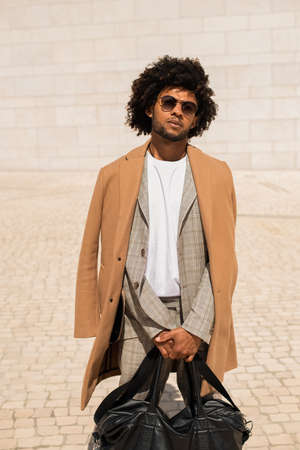 Portrait of African American man with leather bag. Handsome man in suit and coat looking at camera. Portrait, beauty conceptの写真素材