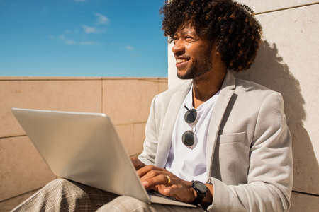 Relaxed African American man working in open air. Man in suit with beard using laptop. Sitting at...