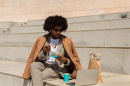 Concentrated African American man having brunch. Man eating salad, drinking coffee while working. Meal, job conceptの写真素材