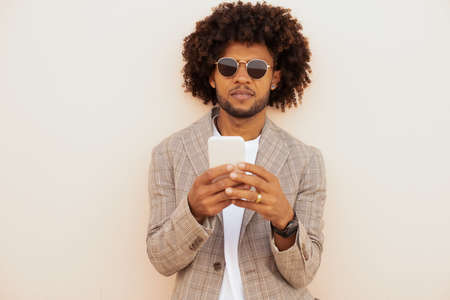 Focused African American man video calling outdoors. Man in suit with beard holding mobile phone. Communication, technology conceptの写真素材