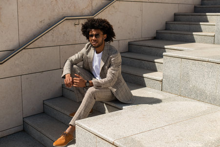 Portrait of good-looking Black man outdoors. African American man in suit sitting on stairs. Portrait, city life conceptの写真素材