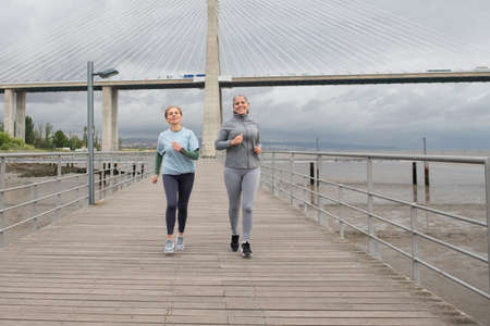 Contented senior friends jogging on embankment. Women in sportive clothes exercising on cloudy day. Sport, friendship conceptの写真素材