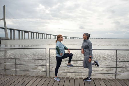 Senior friends resting after training. Women in sportive clothes communicating on embankment on cloudy day. Sport, friendship conceptの写真素材