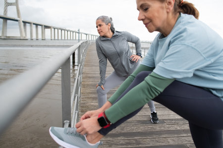 Active senior friends exercising on embankment. Women in sportive clothes stretching on cloudy day. Sport, friendship conceptの写真素材