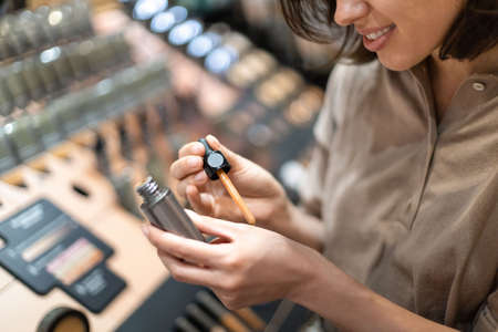 Smiling young woman testing concealer at beauty store. Close-up of pretty girl applying foundation...