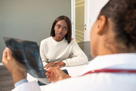 Serious woman having consultation of pulmonoligist in clinic. Young African American female patient...