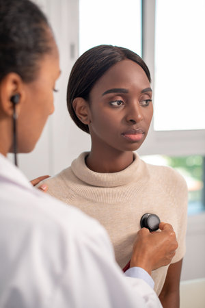 Attentive African American woman at appointment. Female patient sitting on sofa, doctor using...
