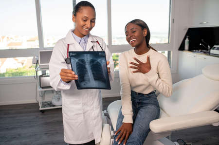 Stress-free African American woman at doctors appointment. Female patient sitting on sofa, doctor showing x-ray photo. Medicine, health conceptの写真素材