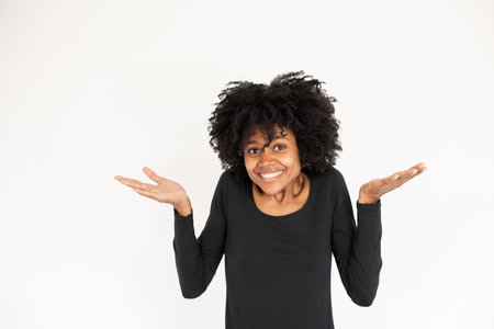 Portrait of embarrassed African American shrugging shoulders. Young female model wearing black dress looking at camera in confusion. Ignorance and excuse conceptの写真素材
