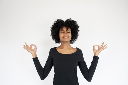 Portrait of peaceful African American woman meditating. Young female model wearing black dress doing...