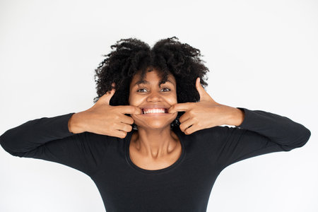 Portrait of funny African American woman teasing showing teeth. Young female model wearing black dress looking at camera and playing fool. Fun and humor conceptの写真素材