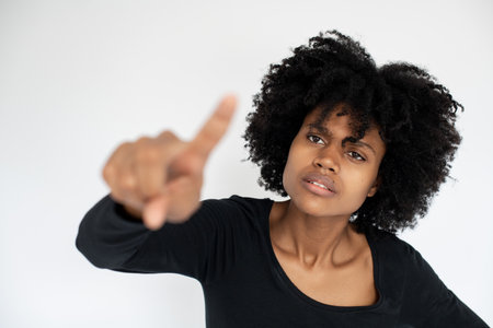 Portrait of concentrated African American woman wiping dirt off camera. Young female model wearing black T-shirt pointing at camera. Accuracy conceptの写真素材