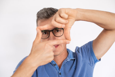 Man in glasses making frame with hands and fingers. Mid adult male model in T-shirt looking at camera. Creativity and photography concept.の写真素材