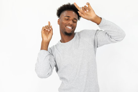 Portrait of carefree African American man dancing. Excited young bearded guy wearing white sweater celebrating success against white background. Dancing and happiness conceptの写真素材