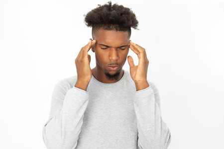 Portrait of stressed African American man touching head. Young bearded guy wearing white sweater suffering from headache or trying to concentrate. Stress or migraine conceptの写真素材