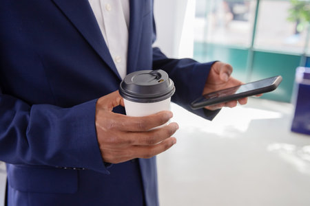 Employee holding disposable cup of coffee and phone in hands. Close-up shot of male office worker...