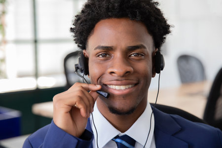 Close up of happy male office worker answering call. Smiling young operator holding microphone, looking at camera. Support, office work concept.の写真素材