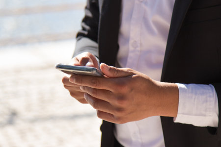 Close-up of male hands with mobile phone. Man holding smart phone browsing internet or reading messages outdoors. Using modern digital technologies conceptの写真素材