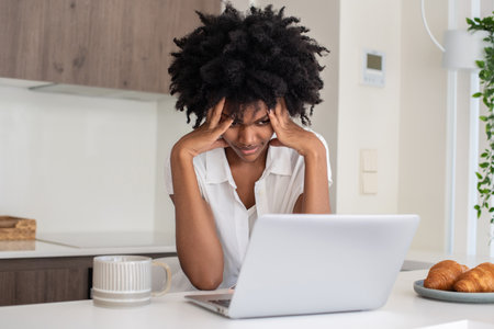 Businesswoman sitting at desk and holding head. Frustrated African American woman thinking, working from home, having problems or difficulties at work. Home office, business, expression conceptの写真素材