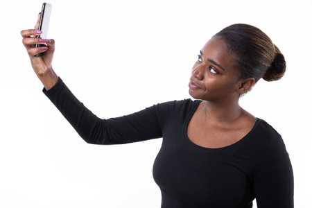 Portrait of concentrated young woman taking selfie with phone. African American lady wearing black...