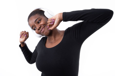 Portrait of happy young woman listening to music in headphones. African American lady wearing black long sleeve looking away and smiling against white background. Leisure and music conceptの写真素材