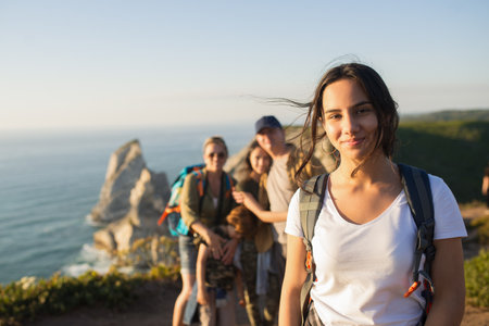 Portrait of smiling teen girl posing on mountain with her family in background. Happy teenager hiking with family in summer. Adolescence and family weekend conceptの写真素材