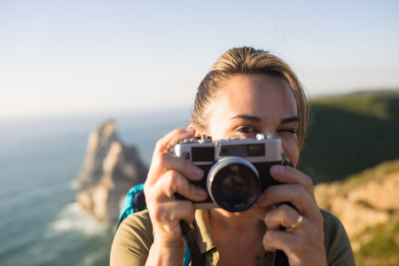 Close-up of mid adult woman with camera outdoors. Happy face of female backpacker taking photo and winking. Travel and photographing conceptの写真素材