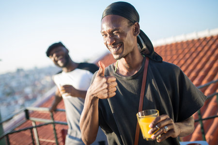Close-up of smiling man posing with glass of useful juice. African man standing with glass of fruit...