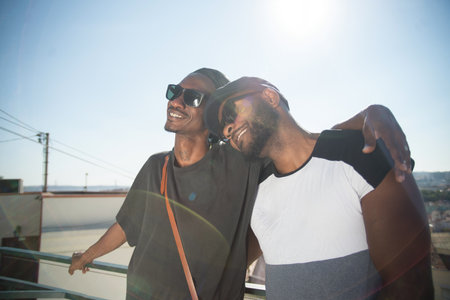 Portrait of happy African gay lovers standing on roof top. Two smiling man feeling joy while dating hugging each other and looking straight. Happiness in relationships and same sex love conceptの写真素材