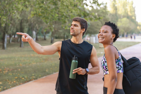 Joggers man and woman talking in park. Man and woman in morning park, man pointing at something, woman laughing. Portrait, sport conceptの写真素材