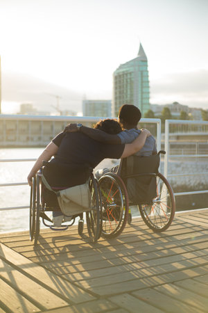 Peaceful biracial family having romantic date. African American man and Caucasian woman in wheelchairs, leaning on shoulder, looking at sunset. Love, affection, happiness conceptの写真素材