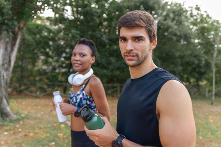 Sportive couple looking at camera in morning park. Man and woman resting from exercises. Portrait, sport conceptの写真素材