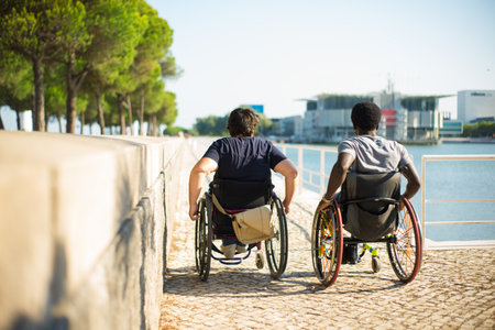 Back view of family in wheelchairs spending time near water. African American man and Caucasian woman in casual clothes, looking forward. Love, affection, happiness conceptの写真素材