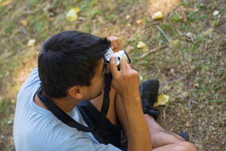 Top view of Asian man with photo camera in summer park. Young man in T-shirt and shorts sitting on...
