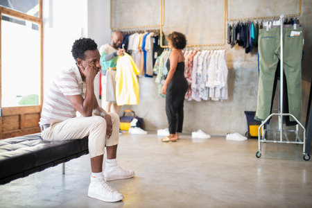 Portrait of African American customers and seller in boutique. Young woman helping bearded man to...