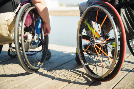 Close-up of colorful wheelchairs. Caucasian female and African American man hands on wheels of wheelchairs during walk in park. Disability conceptの写真素材
