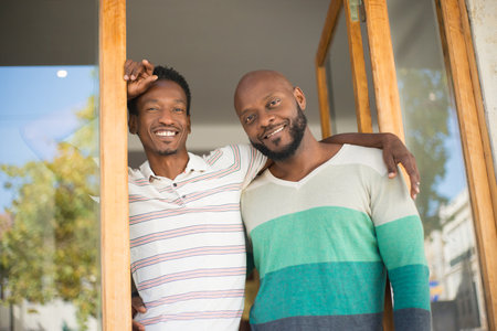 Portrait of African American gay couple at store entrance. Two smiling men standing close hugging looking at camera. Same sex love, leisure activity, buying modern clothes conceptの写真素材