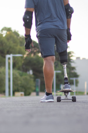 Back view of man with disability skating on summer day. Strong person in casual clothes with prosthetic leg on skateboard. Sport, disability, hobby conceptの写真素材