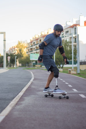 Man with mechanical leg in casual clothes skateboarding. Mid adult sportsman riding down special road in concentration. Sport, disability, training conceptの写真素材