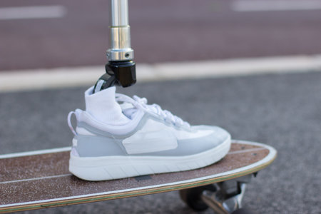 Close-up of mechanical male leg in sneaker on skateboard. White shoes and longboard, man training in park. Sport, disability conceptの写真素材