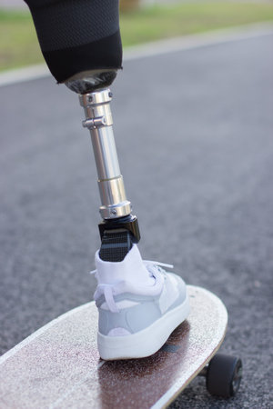 Back view of artificial male leg in sneaker on skateboard. White shoes and longboard, man training...