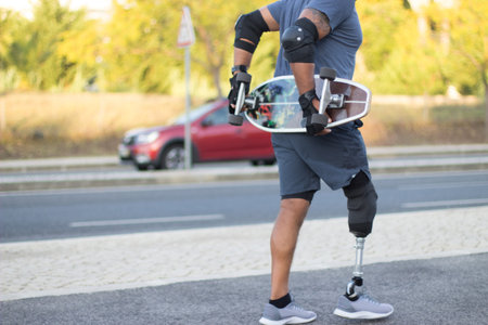 Close-up of man with disability carrying skateboard in park. Strong person with prosthetic leg...