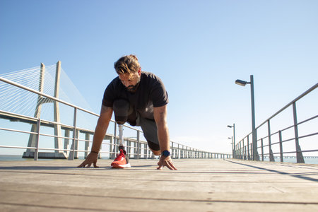 Portrait of man with leg prothesis on start for running. Dark-haired man standing on bridge over sea...