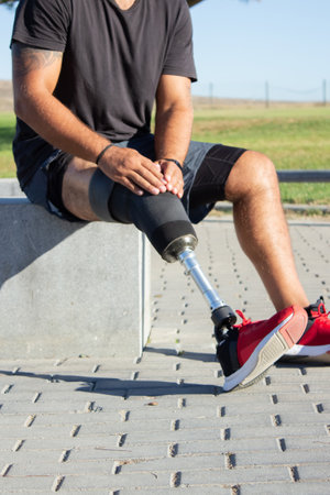 Close-up of male body with prosthetic leg. Trained guy with artificial leg sitting outdoors fixing his prothesis for street workout. Active life of people with disability, sport motivation conceptの写真素材