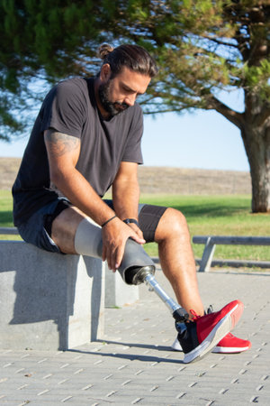 Portrait of man with disability preparing for training. Man sitting outdoors massaging and fixing...