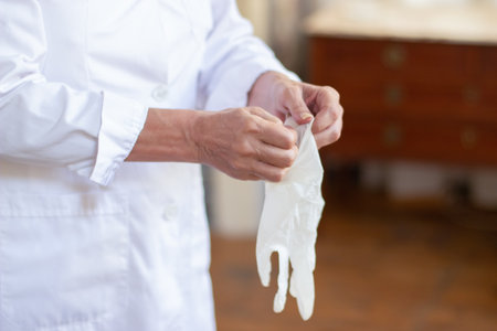 Close-up of skilled female doctors hands holding sterile gloves. Woman in white uniform putting on gloves preparing for medical examination and work. Medical help, consultation and health care conceptの写真素材