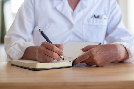 Close-up of professional female doctors hands during pandemic. Woman in medical uniform sitting at table with pen and notebook making notes. Doctors duty, health care, medical service conceptの写真素材